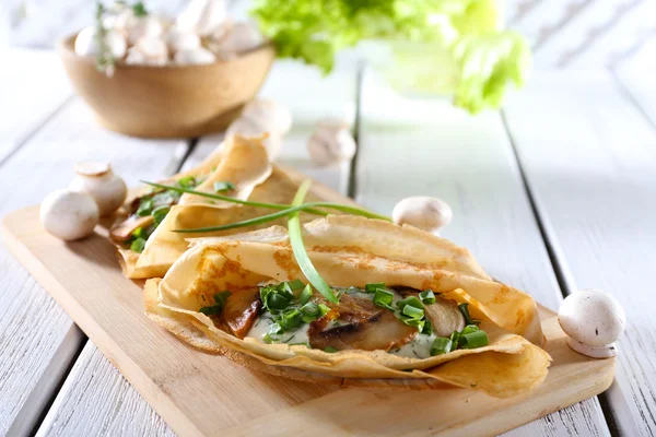 Pancakes with creamy mushrooms on cutting board on wooden table, closeup — Stock Photo, Image