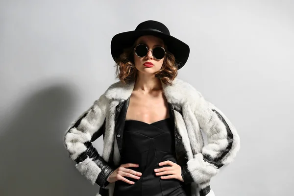Kürk ceket, şapka ve güneş gözlüğü gri arka plan üzerinde güzel model portresi — Stok fotoğraf