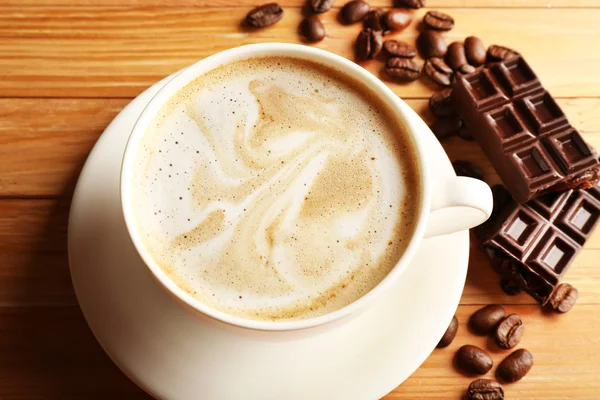 Cup of coffee latte art with grain and chocolate on wooden table, closeup — Stock Photo, Image