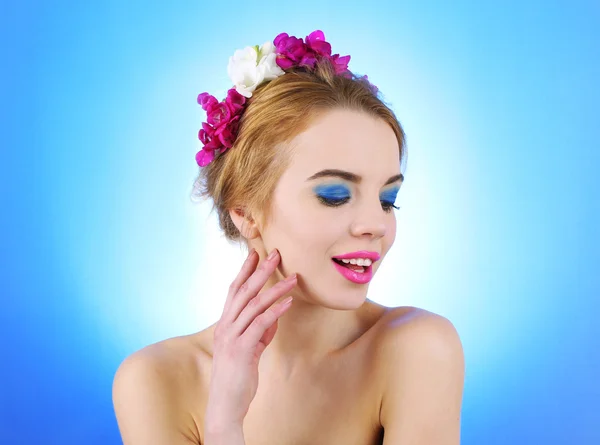 Portrait de jeune femme avec des fleurs dans les cheveux sur fond bleu — Photo