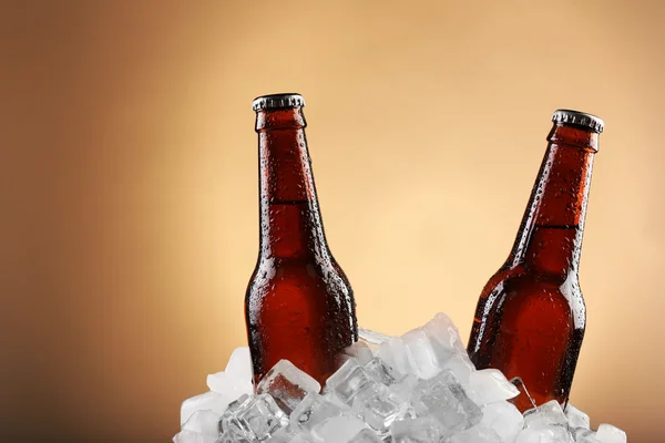 Botellas de vidrio de cerveza en cubos de hielo sobre fondo de color — Foto de Stock