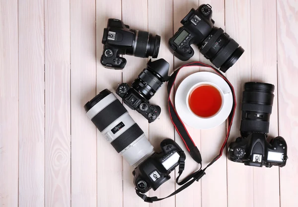 Appareils photo modernes avec tasse de thé sur table en bois, vue sur le dessus — Photo