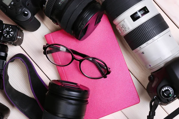 Câmeras modernas com óculos e diário rosa na mesa de madeira, close-up — Fotografia de Stock