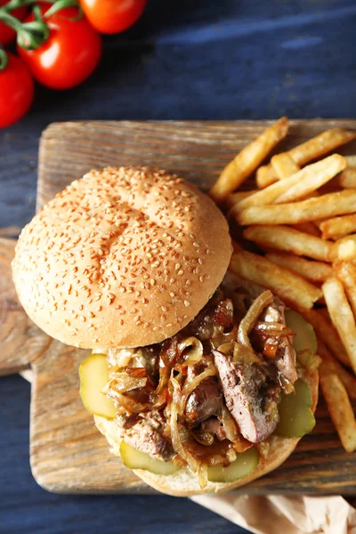 เบอร์เกอร์อร่อยกับเฟรนช์ฟรายส์บนพื้นหลังโต๊ะไม้ แนวคิดอาหารที่ไม่ดีต่อสุขภาพ — ภาพถ่ายสต็อก