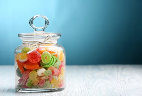 Kleurrijke snoepjes in pot op tafel op blauwe achtergrond — Stockfoto