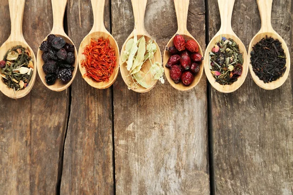 Collection of tea and natural additives in wooden spoons, on old wooden table — Stock Photo, Image