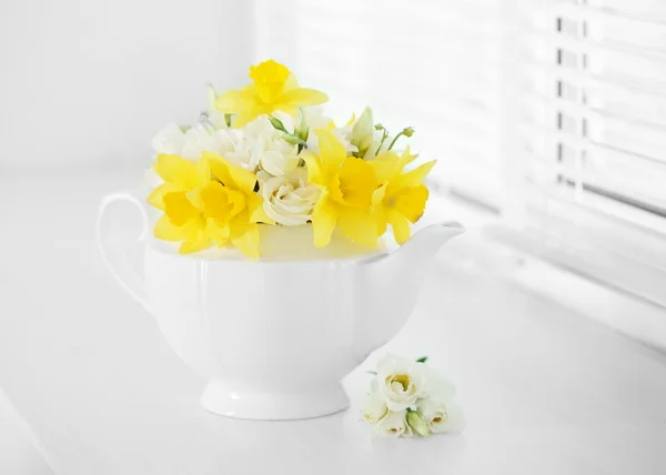 Hermoso ramo de narcisos amarillos y rosas en tetera en el alféizar de la ventana — Foto de Stock