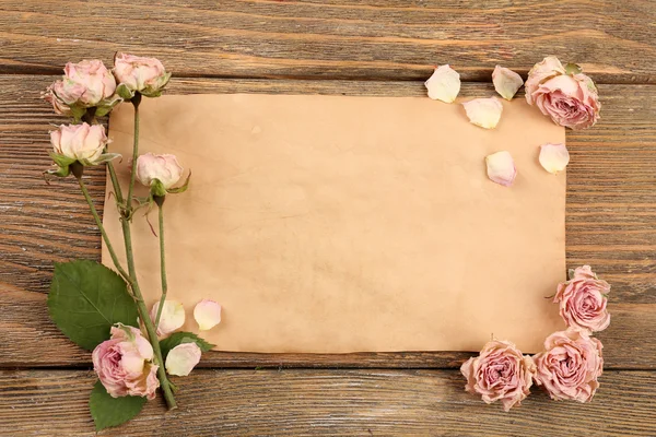 Rosas secas en hoja de papel sobre mesa de madera, vista superior — Foto de Stock