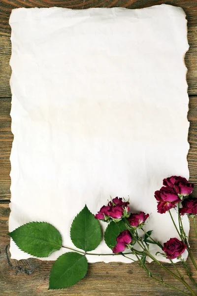 Getrocknete Rosen auf Blatt Papier auf Holztisch, Draufsicht — Stockfoto