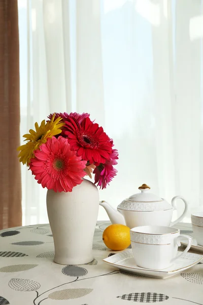 Bunte Gerbera in der Vase mit Teekanne, Tassen und Zitronen auf dem Tisch auf Vorhängen Hintergrund — Stockfoto