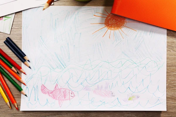 Kids drawing on white sheet of paper with crayons on wooden table, closeup — Stock Photo, Image