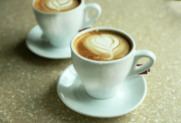 Tazze di cappuccino con cuore su schiuma su tavolo in caffè — Foto Stock