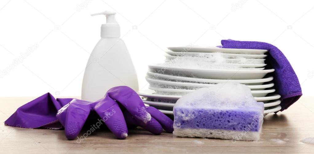 Plates in foam with gloves and cleanser on table isolated on white