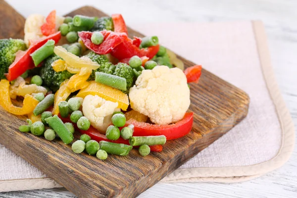 Verduras congeladas sobre tabla de cortar, sobre servilleta, sobre fondo de mesa de madera —  Fotos de Stock