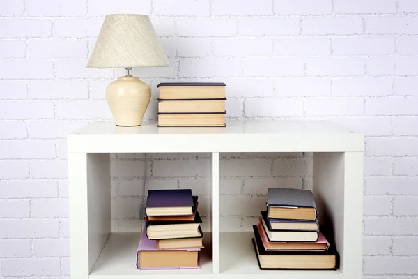 Wooden shelf with books and lamp on brick wall background