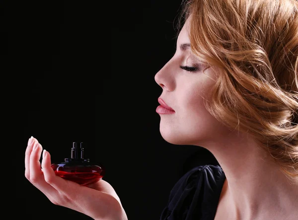 Piękna młoda kobieta z butelki perfum na czarnym tle — Zdjęcie stockowe
