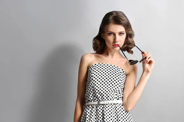 Portret van mooie model uitgedrukt in dots jurk in zonnebril op grijze achtergrond — Stockfoto