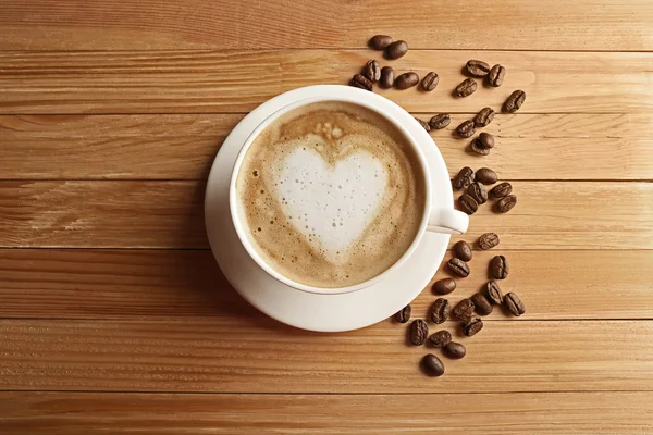 Tasse de café latte art avec des grains sur table en bois, vue sur le dessus — Photo