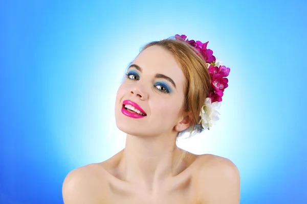 髪に青色の背景色の花を持つ若い女性の肖像画 — ストック写真