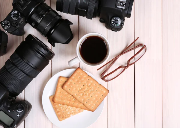 Moderne camera's met een bril, kopje koffie en koekjes op houten tafel, top weergave — Stockfoto