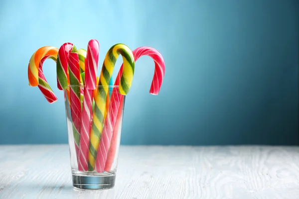 Coloridos bastones de caramelo en vidrio sobre la mesa sobre fondo azul —  Fotos de Stock