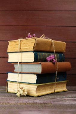 Stack of books with dry flowers on wooden background clipart