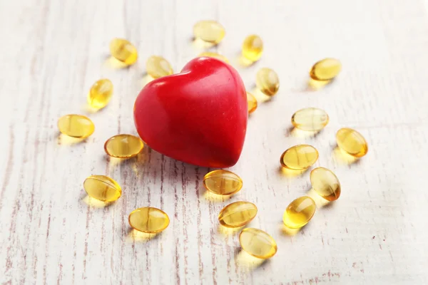 Red heart and cod liver oil, on wooden background — Stock Photo, Image