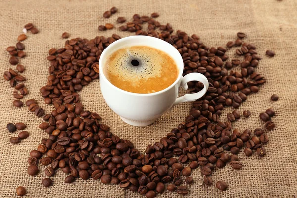 Φλιτζάνι καφέ με κόκκους σε λινάτσα ύφασμα φόντο — Φωτογραφία Αρχείου