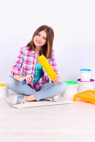 Hermosa chica sentada en el suelo con el equipo para pintar la pared —  Fotos de Stock