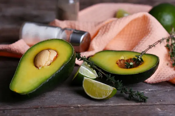 Sliced avocado with lime, salt and pepper on napkin on wooden background — Stock Photo, Image