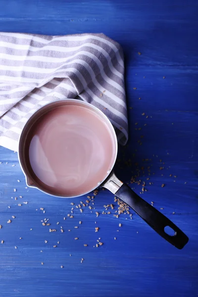 Metal pot of cocoa with sugar and napkin on color wooden background — Stock Photo, Image