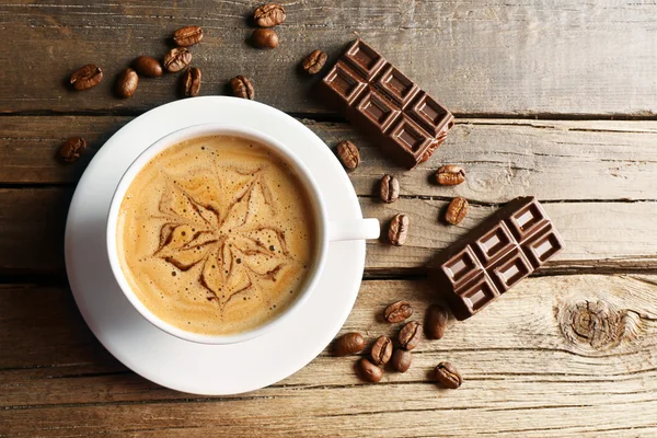 Cup of coffee latte art with grains and chocolate on wooden table, top view — Stock Photo, Image