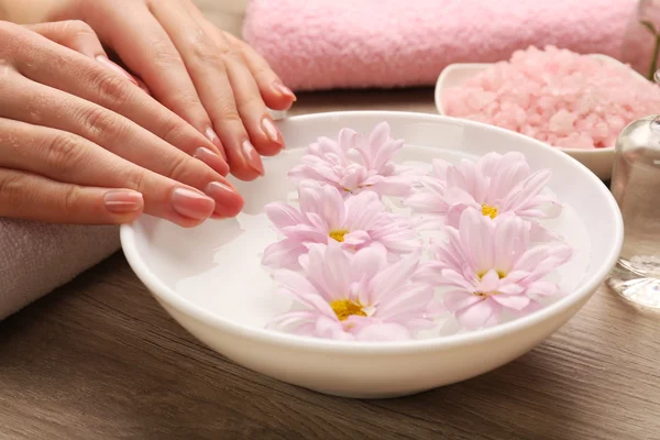 Mãos femininas e tigela de água termal com flores, close-up — Fotografia de Stock
