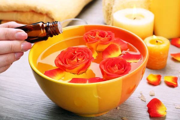 Vrouwelijke hand met fles essentie en kom van het aroma spa water op houten tafel, close-up — Stockfoto