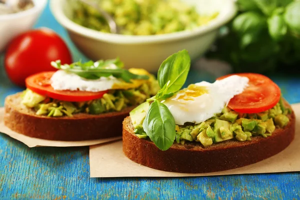 Tasty sandwich with egg, avocado and vegetables on paper napkin, on color wooden background — Stock Photo, Image