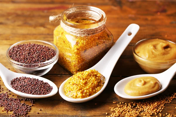 Mustard seeds, powder and sauce in spoons, bowls and glass jar on wooden background — Stock Photo, Image