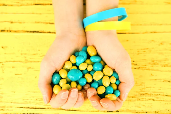 Manos con caramelos azul-amarillos - colores de la bandera de Ucrania, sobre fondo de madera — Foto de Stock