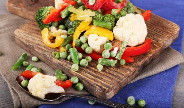 Frozen vegetables on cutting board, on napkin, on wooden table background — Stock Photo, Image