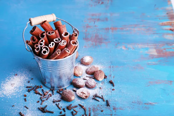 Cinnamon sticks in metal bucket, nutmeg and cloves on color wooden table background — Stock Photo, Image