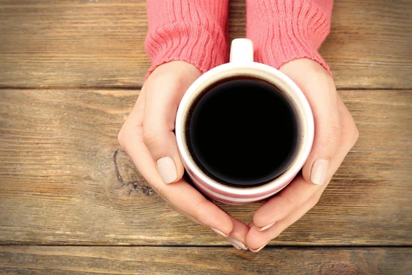 Mani femminili che tengono la tazza di caffè su sfondo di legno — Foto Stock