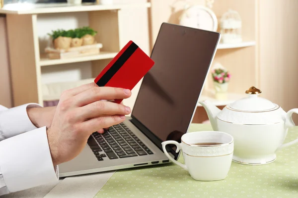 Man houden creditcard en werken op laptop op huis interieur achtergrond — Stockfoto