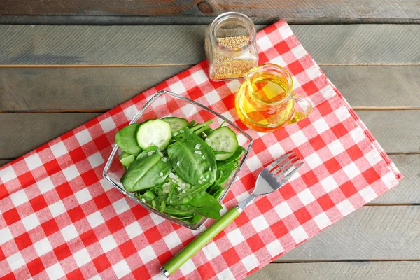 Cuenco de vidrio de ensalada verde con pepino y espinacas en mesa de madera con servilleta, primer plano —  Fotos de Stock