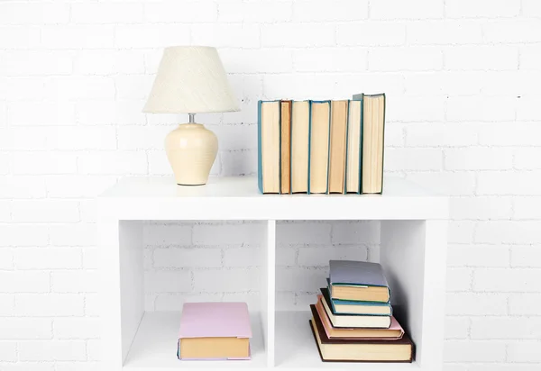 Wooden shelf with books and lamp on brick wall background — Stock Photo, Image