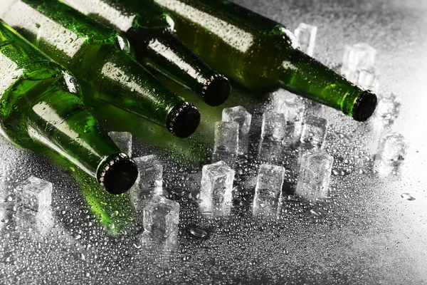 Bottiglie di vetro di birra con cubetti di ghiaccio su sfondo tavolo bagnato — Foto Stock