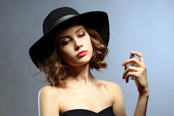 Hermosa mujer con frasco de perfume sobre fondo gris — Foto de Stock