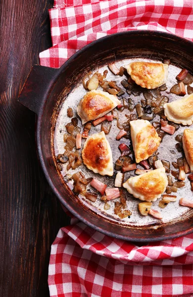 Pierogi smażone z cebulą i boczkiem w patelni, na tle drewniany stół — Zdjęcie stockowe