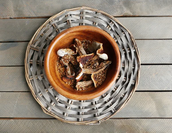 Gedroogde champignons in kom op rieten mat op houten tafel, bovenaanzicht — Stockfoto