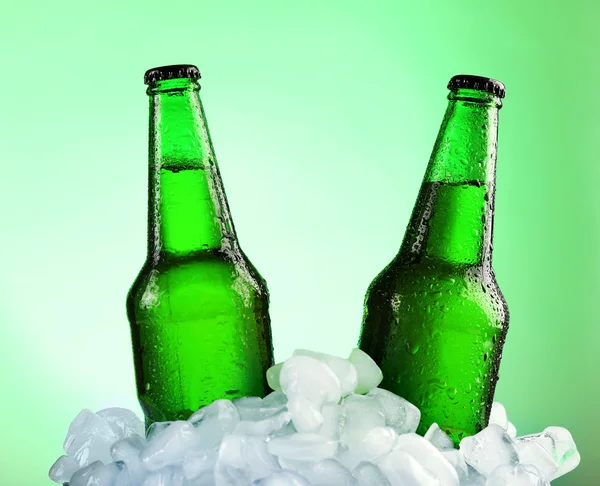 Glazen flessen bier in ijsblokjes op kleur achtergrond — Stockfoto