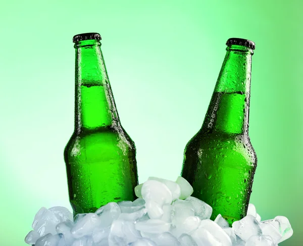 Botellas de vidrio de cerveza en cubos de hielo sobre fondo de color — Foto de Stock