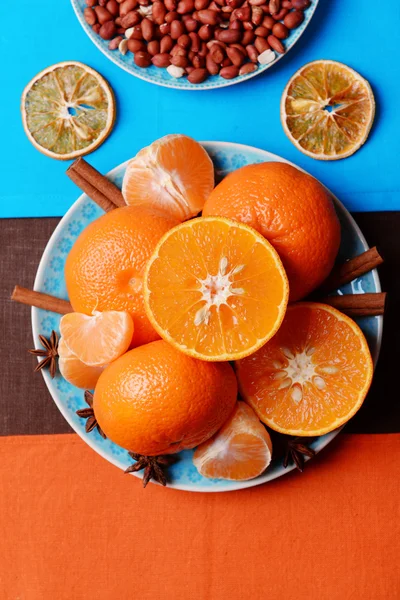 オレンジ色のみかん、ピーナッツ、青い木製のテーブルの上にシナモンスティックを表示します。 — ストック写真